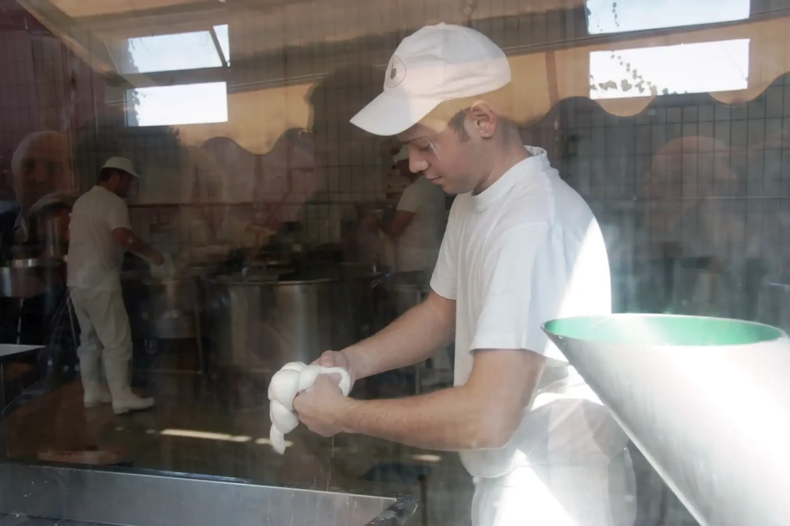 Ein junger Mann hält in der Produktion einen Mozzarella di Bufala in den Händen.