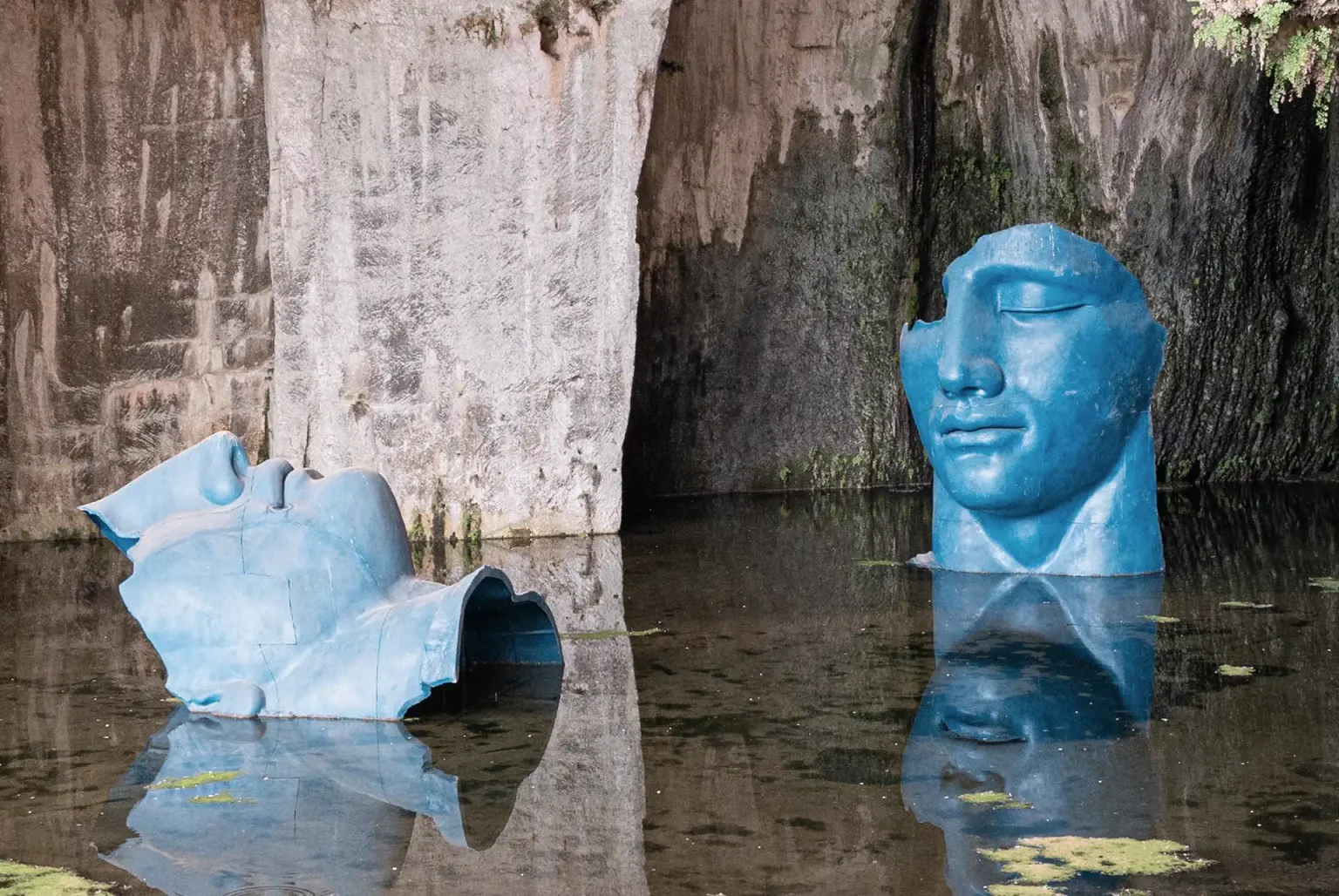 Kunstwerk: Köpfe in einer Höhle liegend, halb im Wasser